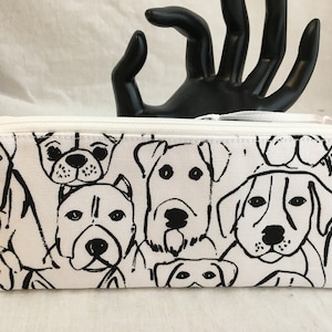 May include: A rectangular pencil case with a white background and a repeating black line drawing of various dog breeds. The case has a white zipper and a small white loop. The overall design is simple and graphic.