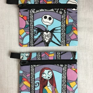 May include: Two small zippered pouches with a stained glass pattern featuring Jack Skellington and Sally from The Nightmare Before Christmas. The pouches are made of fabric and have black zippers.