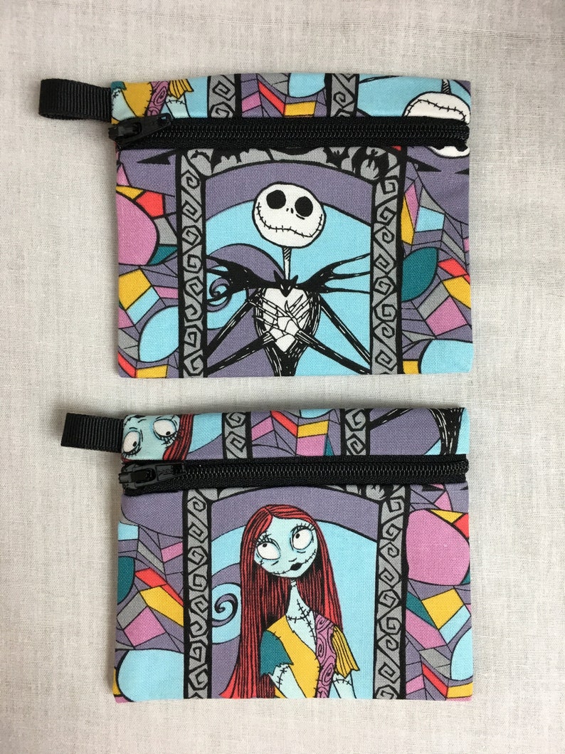 May include: Two small zippered pouches with a stained glass pattern featuring Jack Skellington and Sally from The Nightmare Before Christmas. The pouches are made of fabric and have black zippers.