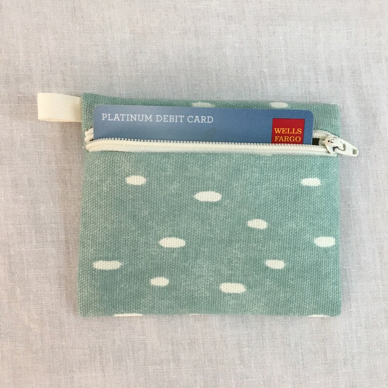 May include: A small, green zippered pouch with white polka dots. A credit card with the text "PLATINUM DEBIT CARD" and "WELLS FARGO" is partially visible inside the pouch.