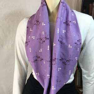 May include: A purple infinity scarf with a white and purple geometric pattern and a repeating image of dancers in a purple silhouette.