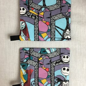 May include: Two fabric pouches with a black zipper and a black strap. The pouches are printed with a colorful stained glass pattern featuring characters from the Nightmare Before Christmas. The characters include Jack Skellington and Sally.