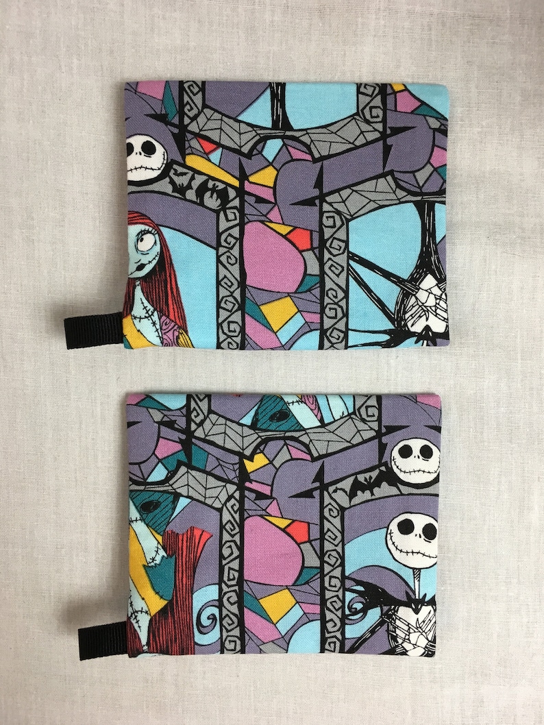 May include: Two fabric pouches with a black zipper and a black strap. The pouches are printed with a colorful stained glass pattern featuring characters from the Nightmare Before Christmas. The characters include Jack Skellington and Sally.