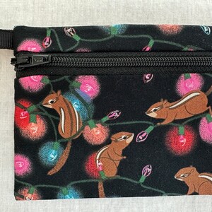 May include: A black zippered pouch with a colorful print of chipmunks and Christmas lights. The pouch has a black zipper and a black strap.