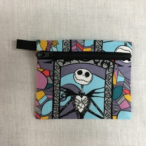 May include: A small zippered pouch with a colorful stained glass pattern featuring Jack Skellington from The Nightmare Before Christmas. The pouch is made of fabric and has a black zipper.