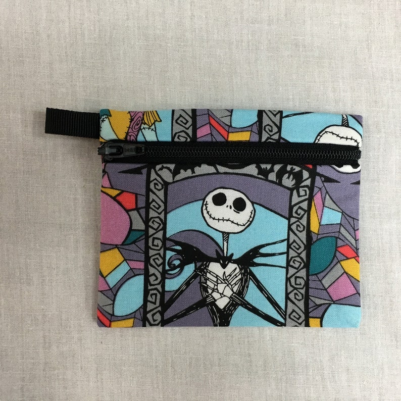 May include: A small zippered pouch with a colorful stained glass pattern featuring Jack Skellington from The Nightmare Before Christmas. The pouch is made of fabric and has a black zipper.