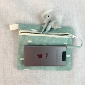May include: A teal zippered pouch with white polka dots, containing a silver iPod with the Apple logo and the word "iPod" printed on it.  A pair of white earbuds are partially sticking out of the pouch.