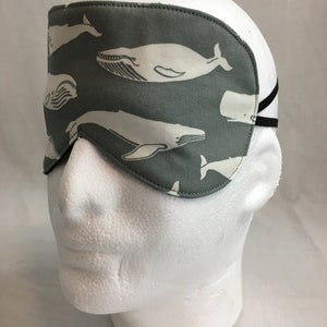 Puede incluir: Una m&aacute;scara para dormir gris con un patr&oacute;n de ballena blanca. La m&aacute;scara tiene una banda el&aacute;stica para sujetarla a la cabeza.