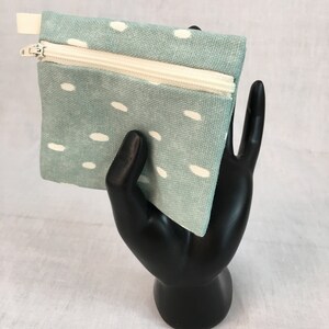 May include: A small, light blue zippered pouch with a white polka dot pattern. The pouch is made of fabric and has a white zipper.