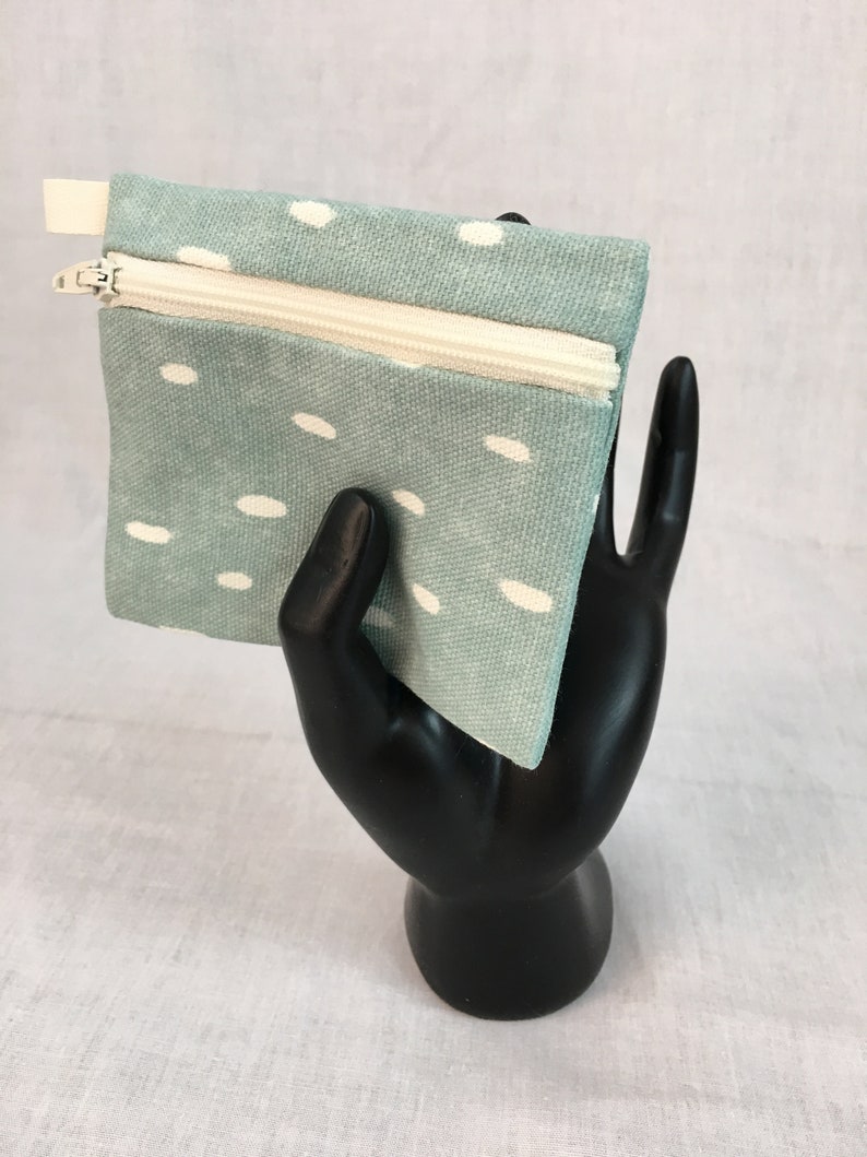 May include: A small, light blue zippered pouch with a white polka dot pattern. The pouch is made of fabric and has a white zipper.