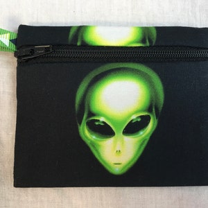 May include: A black zippered pouch with a green alien face graphic print. The pouch has a green and white patterned zipper pull.