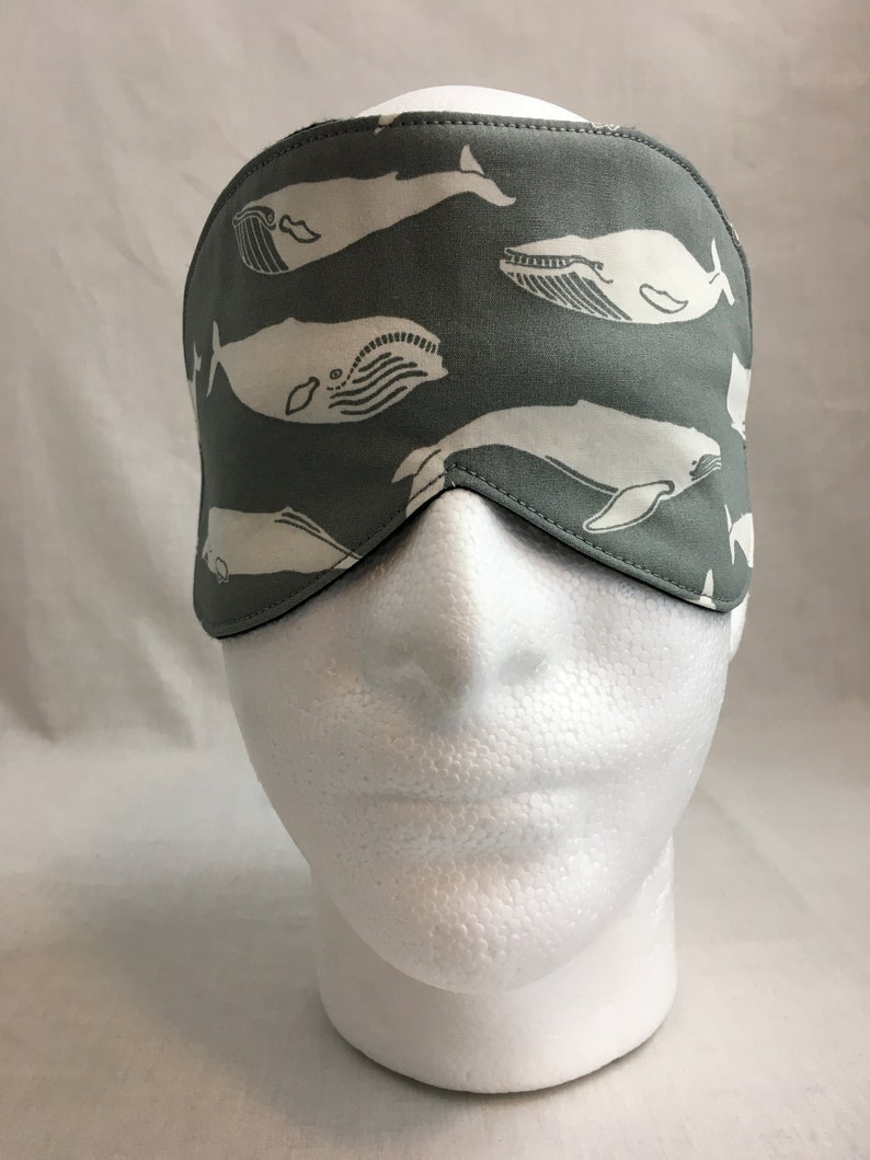 Puede incluir: Una m&aacute;scara para dormir gris con un patr&oacute;n de ballena blanca. La m&aacute;scara est&aacute; hecha de tela suave y tiene una correa el&aacute;stica.