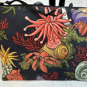 May include: Black zippered pouch with a colorful sea life print. The print features red and pink anemones, yellow and orange starfish, and red and brown hermit crabs.