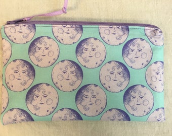 May include: A green zippered pouch with a repeating pattern of purple and white moons with faces.