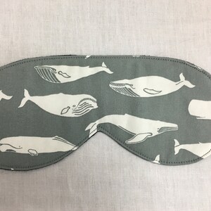 Puede incluir: Una m&aacute;scara para dormir gris con un patr&oacute;n de ballena blanca. La m&aacute;scara est&aacute; hecha de tela suave y tiene una correa el&aacute;stica.