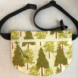 May include: A small, cream-colored fanny pack with a zipper closure and a black adjustable strap. The fanny pack has a green and brown print of stylized trees.