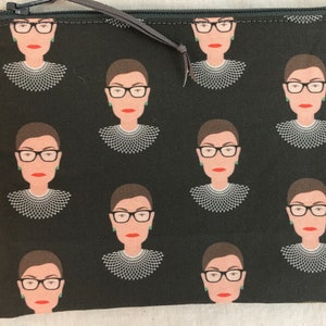 May include: Black zippered pouch with a repeating pattern of a woman wearing glasses and a white collar. The woman is depicted in a minimalist style.