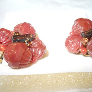 May include: A pair of red and brown clip-on earrings with a cluster of small, round beads. The beads have a textured surface and are accented with small, clear rhinestones.