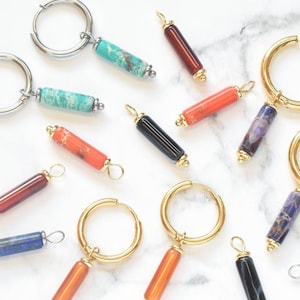 May include: A collection of hoop earrings and individual cylindrical stone charms in various colours including turquoise, red, orange, blue, purple, and black. The hoops are made of silver-toned and gold-toned metal, featuring smooth stone beads.