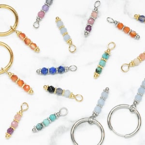 Può includere: Assortimento di ciondoli con perline di pietre preziose colorate con anelli a salto dorati. I ciondoli sono infilati su una catena d'argento e sono perfetti per aggiungere un tocco di colore e personalità a qualsiasi progetto di gioielleria.