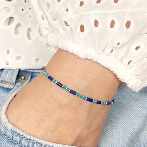 Könnte beinhalten: Ein zartes Armband aus kleinen blauen und türkisfarbenen Perlen. Das Armband befindet sich am Handgelenk.