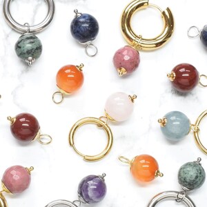 Peut inclure: Une collection de boucles d'oreilles créoles et de perles en pierre gemme individuelles de diverses couleurs, dont rose, vert, bleu, orange, violet et rouge. Les créoles sont en métal doré et argenté, avec des breloques en pierre polie.