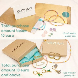 May include: Two brown cardboard boxes with the text "NOZUNO SPARKLING JEWELRY" on the top. The boxes are filled with colourful beaded jewellery, including necklaces, bracelets, and earrings. The text "Total purchase amount below 10 euro" is on the top box and "Total purchase amount 10 euro and above" is on the bottom box. The boxes are labelled as "Eco-friendly paper bag" and "Eco-friendly jewellery box".