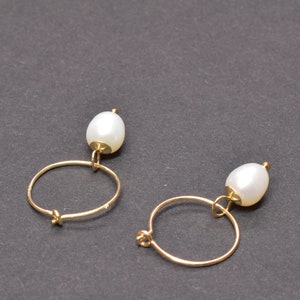 May include: A pair of gold hoop earrings with a single white pearl dangling from each hoop.
