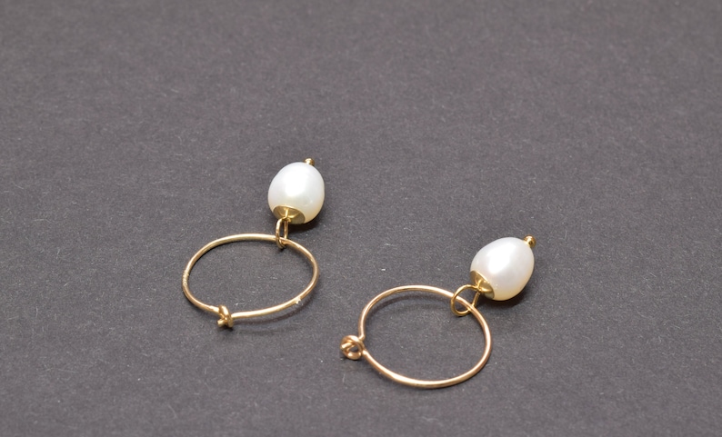 May include: A pair of gold hoop earrings with a single white pearl dangling from each hoop.