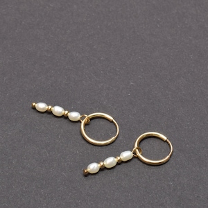 May include: A pair of gold hoop earrings with a row of white pearls dangling from each hoop.