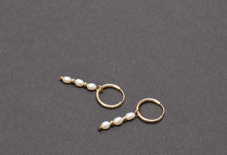 May include: A pair of gold hoop earrings with a row of white pearls dangling from each hoop.