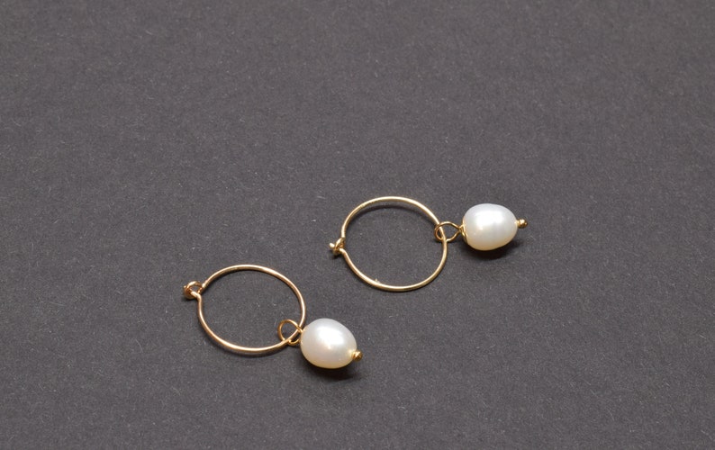 May include: A pair of gold hoop earrings with a single white pearl dangling from each hoop.