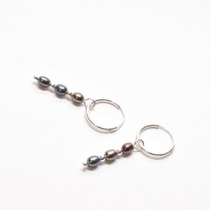 May include: A pair of silver hoop earrings with a dangling strand of three dark grey pearls.