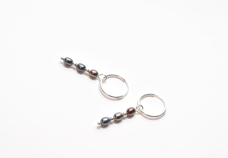 May include: A pair of silver hoop earrings with a dangling strand of three dark grey pearls.