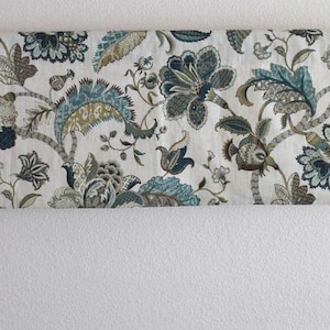 May include: A white valance with a floral pattern in shades of blue, green, and brown. The valance has a rod pocket and is hung on a white wall.