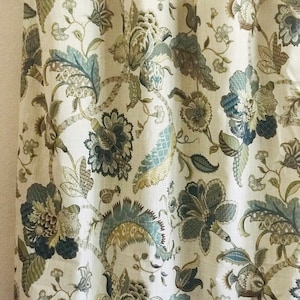 May include: A white curtain with a floral pattern in shades of brown, blue, and green. The pattern features intricate designs of leaves and flowers.