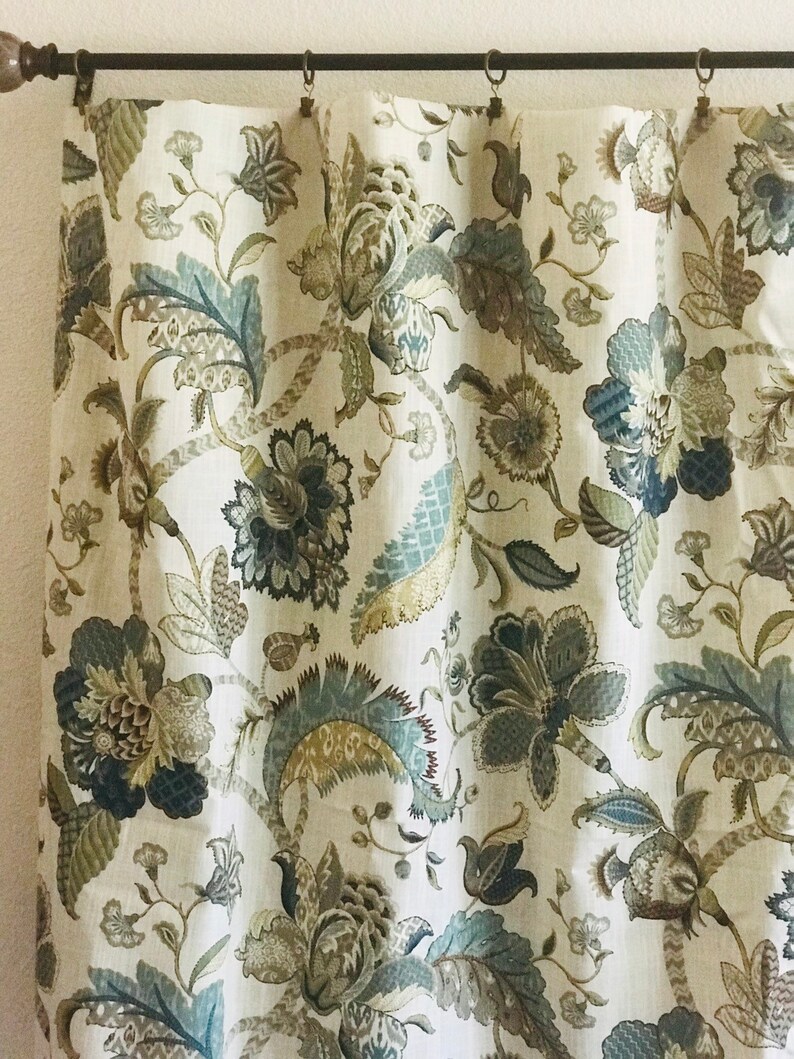 May include: A white curtain with a floral pattern in shades of brown, blue, and green. The pattern features intricate designs of leaves and flowers.