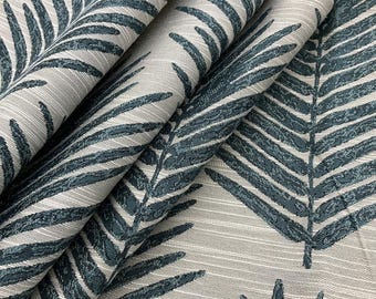 Può includere: Primo piano di un tessuto con un motivo ripetuto di foglie di felce verde acqua su sfondo grigio chiaro. Il tessuto è piegato, mostrando la trama e il design. Le foglie hanno venature dettagliate.