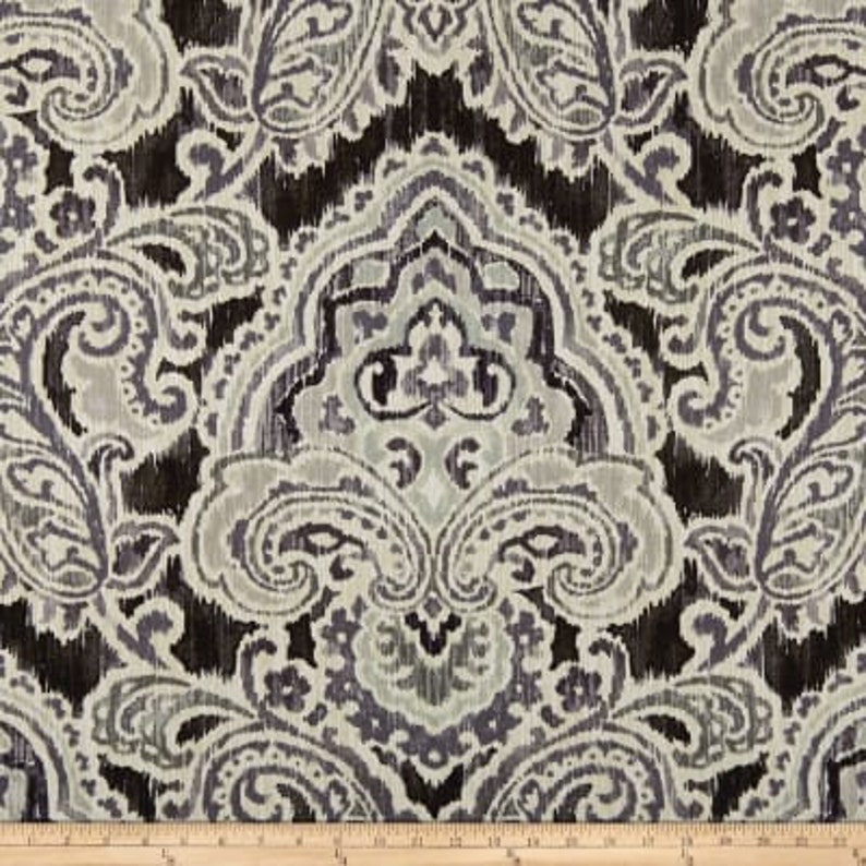 K&ouml;nnte beinhalten: Ein schwarzer und wei&szlig;er Stoff mit Paisley-Muster und einem dezenten Glanz. Der Stoff zeigt ein gro&szlig;es, kompliziertes Paisley-Muster in der Mitte, umgeben von kleineren Paisley-Motiven.