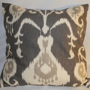 Pode incluir: Uma almofada de lançamento cinza e branca com um design ikat. A almofada é feita de um tecido macio e texturizado.