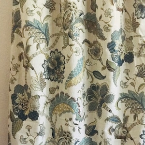May include: A pair of beige linen curtains with a floral pattern in shades of blue, brown, and green. The curtains have a traditional design with intricate details.