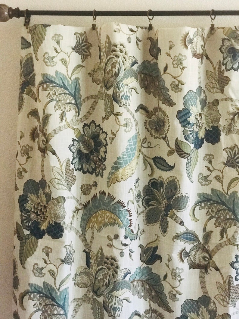May include: A pair of beige linen curtains with a floral pattern in shades of blue, brown, and green. The curtains have a traditional design with intricate details.