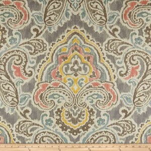 K&ouml;nnte beinhalten: Ein Stoffmuster mit einem Paisley-Muster in Graut&ouml;nen, Blau, Gelb und Rosa. Der Stoff hat einen dezenten Glanz und eine weiche Textur.