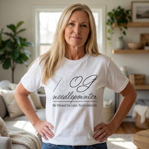 May include: White t-shirt with the text "OG needlepointer" in black script, featuring a needle and thread design. The shirt also includes the phrase "We followed the rules. You're welcome." A woman is wearing the shirt.