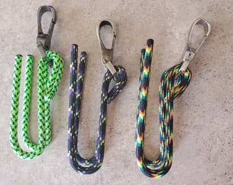 May include: Three colorful paracord lanyards with silver metal clips. The lanyards are green and black, black and purple, and black, orange, and blue.
