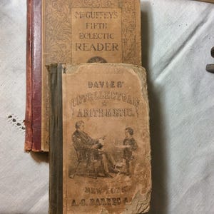 May include: Two antique hardcover books with worn tan covers. The top book is titled McGuffey's Fifth Eclectic Reader. The bottom book is titled Davies' Intellectual Arithmetic and features a black and white illustration of a seated adult and a child.
