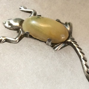 May include: A silver lizard brooch with a pale yellow oval cabochon gemstone.