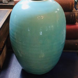 May include: A smooth, rounded ceramic vase with a glossy turquoise glaze. The vase features a narrow circular opening at the top and a bulbous body that tapers slightly toward the base, showcasing a consistent light blue-green color throughout.