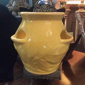 May include: A bright yellow ceramic strawberry planter with a glossy, crackled glaze finish. The pot features a wide, flared rim and two distinct side pockets for planting. The base of the vessel has a molded, textured design around the bottom.