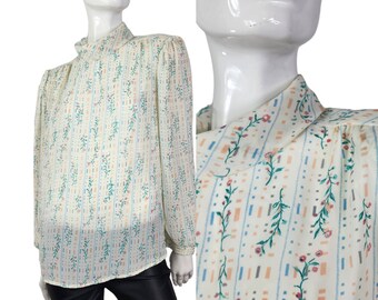 Puede incluir: Una blusa blanca de manga larga con cuello alto y estampado floral. El estampado presenta pequeñas flores rosas, azules y verdes sobre un fondo blanco con finas rayas verticales.